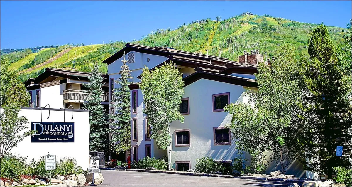 This exterior image showcases the building's welcoming facade, surrounded by a beautifully landscaped garden and clear signage. The backdrop includes mountain views, and the space is clearly connected to both winter and summer activities, like skiing and hiking, as referenced in the section.