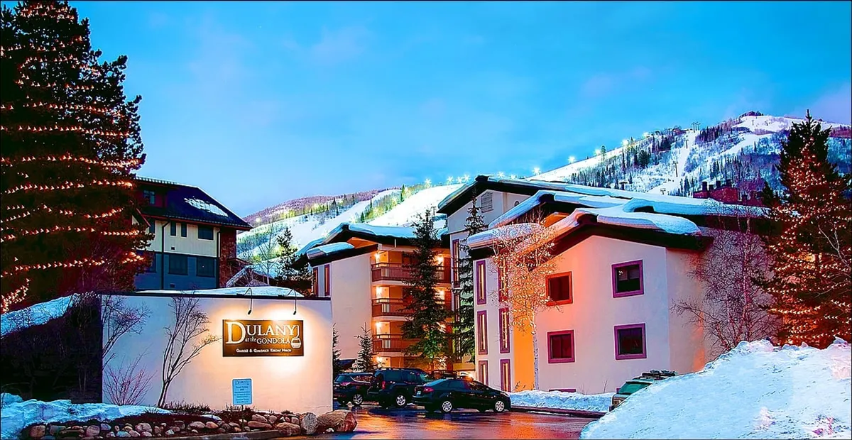 The image highlights the resort's entrance area, featuring the Dulany sign, snow-covered buildings, and a picturesque mountain backdrop. The festive, wintery vibe ties in perfectly with the idea of snowy returns and winter adventures.
