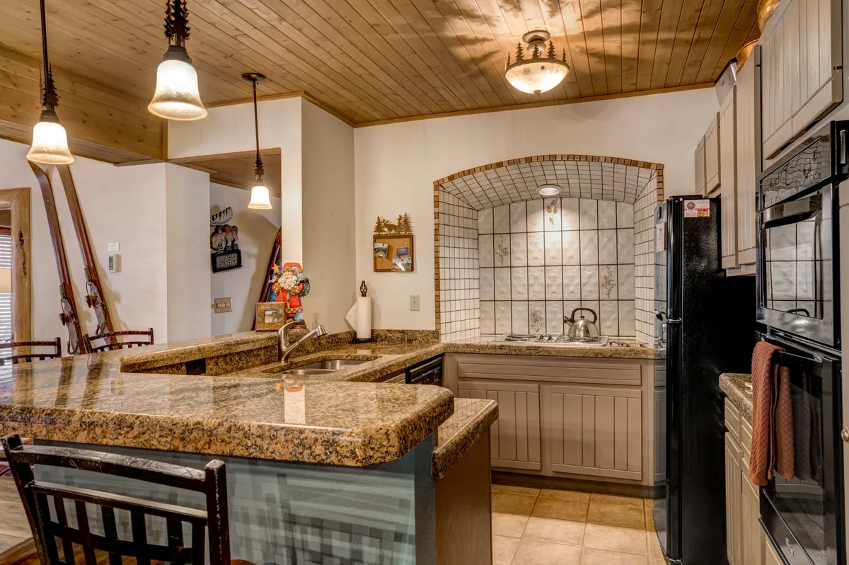 A beautifully upgraded kitchen featuring a granite countertop, a spacious kitchen island, an arched tile backsplash, and hanging pendant lights. The scene is set for entertaining, with ample space for preparing meals and gathering around the central island.