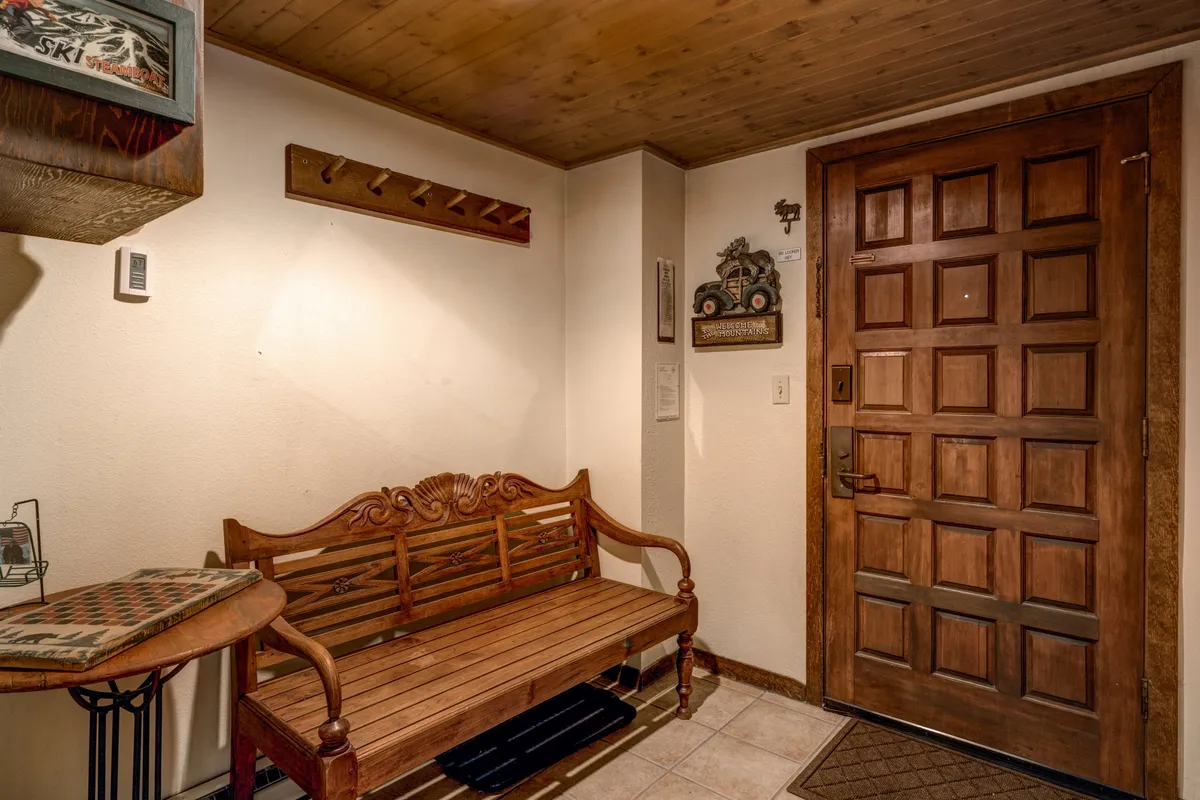 A welcoming entryway with a wooden bench, decorative wall hooks for gear, an ornate door, and a small shelf with decor. The space suggests practicality and warmth, ideal for storing ski gear and starting or ending your mountain adventures.