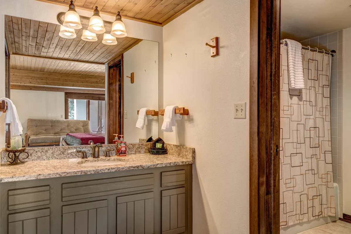 A modern bathroom with granite countertops, a stylish sink and fixtures, a decorative mirror, and a glimpse of the shower area. Sunlight filters through the window, enhancing the clean, calming atmosphere.